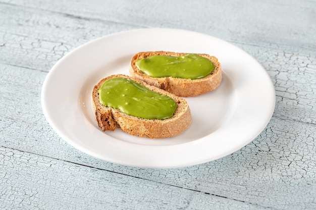 Dos tostadas con mantequilla de pistacho en la placa blanca.