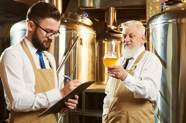 Dos trabajadores de cervecería examinando cerveza artesanal