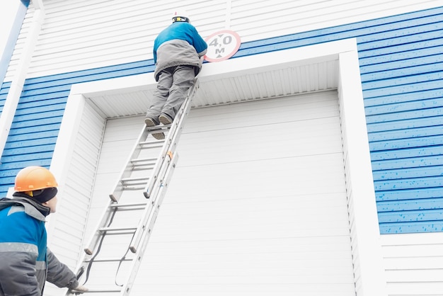 Dos trabajadores de la construcción arreglan el letrero en la puerta automática del garaje para vehículos grandes