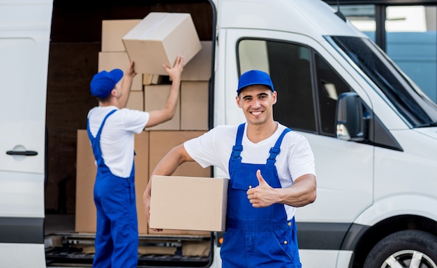 Dos trabajadores de la empresa de mudanzas descargando cajas del minibús al nuevo hogar