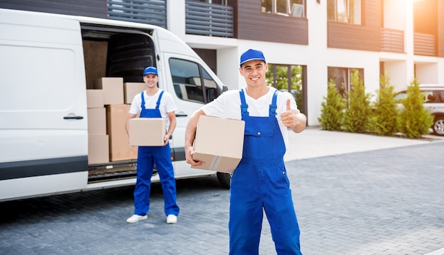 Dos trabajadores de la empresa de mudanzas descargando cajas del minibús al nuevo hogar