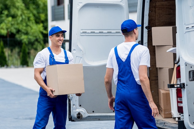 Dos trabajadores de la empresa de mudanzas descargando cajas del minibús al nuevo hogar