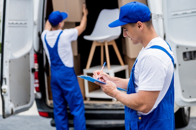 Dos trabajadores de la empresa de mudanzas descargando cajas del minibús al nuevo hogar