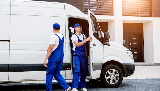 Dos trabajadores de la empresa de mudanzas descargando cajas del minibús al nuevo hogar