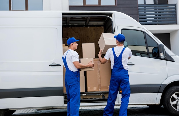 Dos trabajadores de la empresa de mudanzas descargando cajas del minibús al nuevo hogar