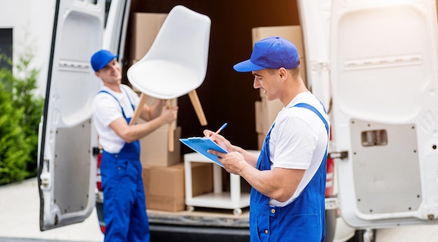 Dos trabajadores de la empresa de mudanzas descargando cajas del minibús al nuevo hogar