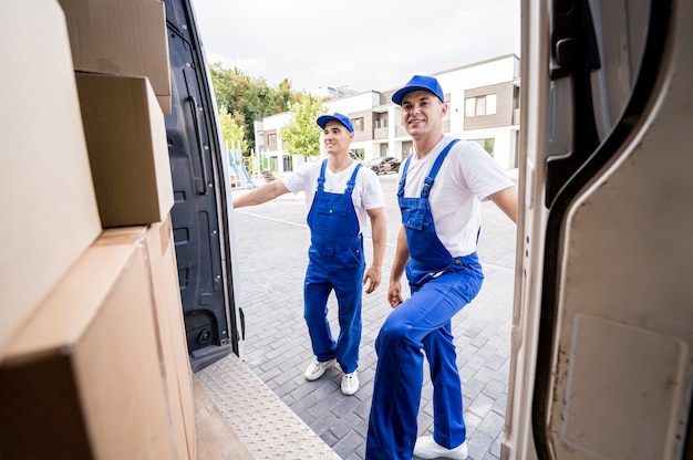 Dos trabajadores de la empresa de mudanzas descargando cajas de minibús