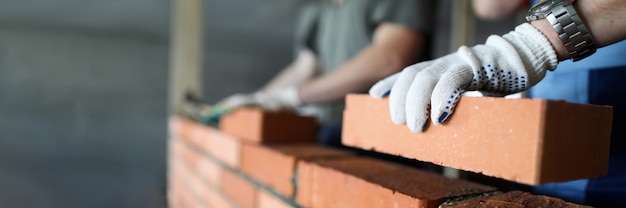 Dos trabajadores haciendo pared de ladrillo rojo en primer plano del sitio de construcción