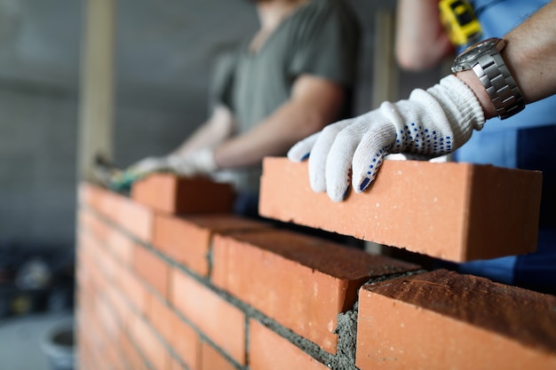 Foto dos trabajadores haciendo pared de ladrillo rojo en primer plano del sitio de construcción