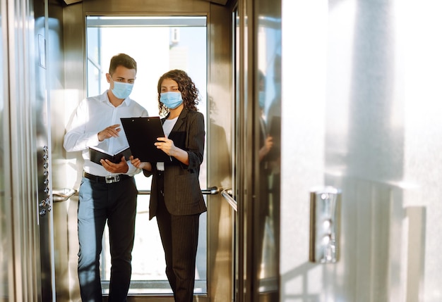 Dos trabajadores con mascarillas protectoras discutiendo el proyecto Trabajar en la oficina durante la cuarentena