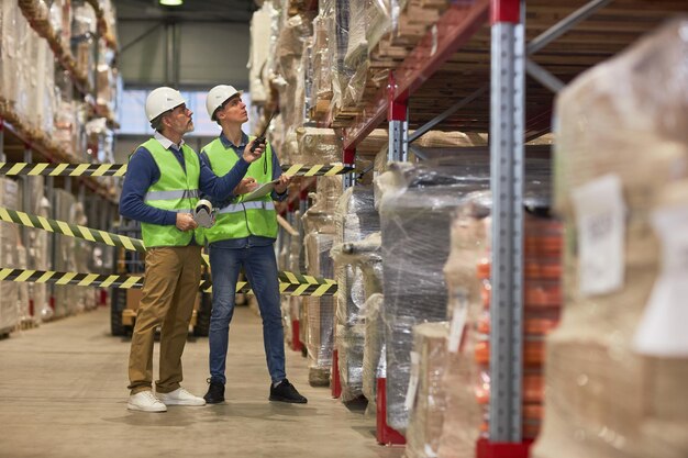 Dos trabajadores masculinos que miran los estantes en el almacén durante la inspección de revisión de existencias