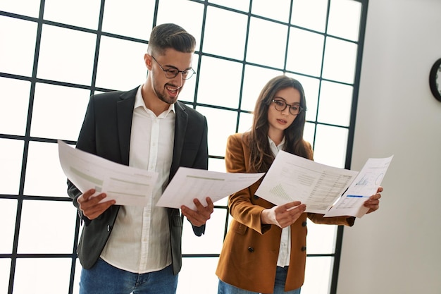 Dos trabajadores de negocios sonriendo felices leyendo papeleo de pie en la oficina.