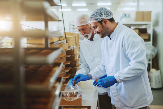 Foto dos trabajadores de una planta de alimentos con uniformes estériles empacando galletas en cajas.