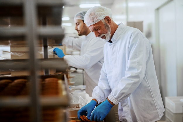 Dos trabajadores de una planta de alimentos con uniformes estériles empacando galletas en cajas.