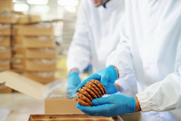 Dos trabajadores de una planta de alimentos con uniformes estériles empacando galletas en cajas.