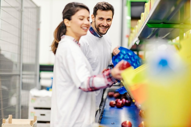 Dos trabajadores de producción de frutas recolectando manzanas de la cinta transportadora