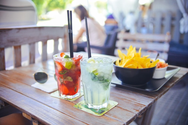 Dos tragos en una mesa con un tazón de papas fritas en la mesa