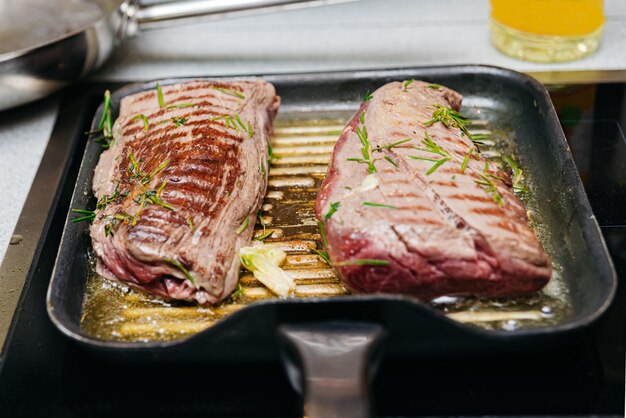 Foto dos trozos de filete de res en una sartén a la parrilla con ajo de mantequilla y romero