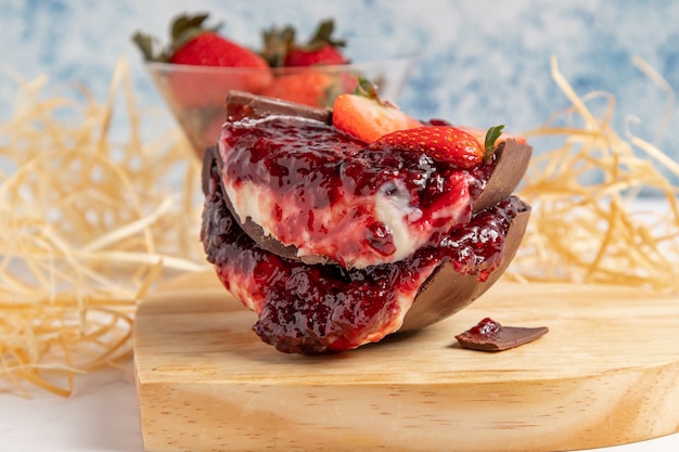 Dos trozos de huevo de pascua rellenos en rodajas con un jugoso relleno de mermelada de fresa capa de galleta capa de chocolate y crema Y un cuenco lleno de fresas en el fondo