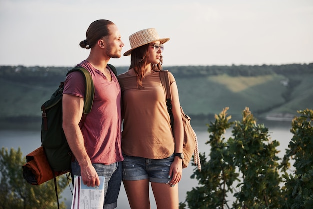 Dos turistas hombres y mujeres con mochilas se colocan en la cima de la peña y disfrutan del amanecer. Viajando montañas y costa, libertad y concepto de estilo de vida activo