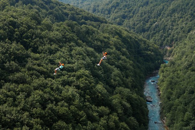 Dos turistas en una tirolesa con el telón de fondo de verdes montañas y ríos