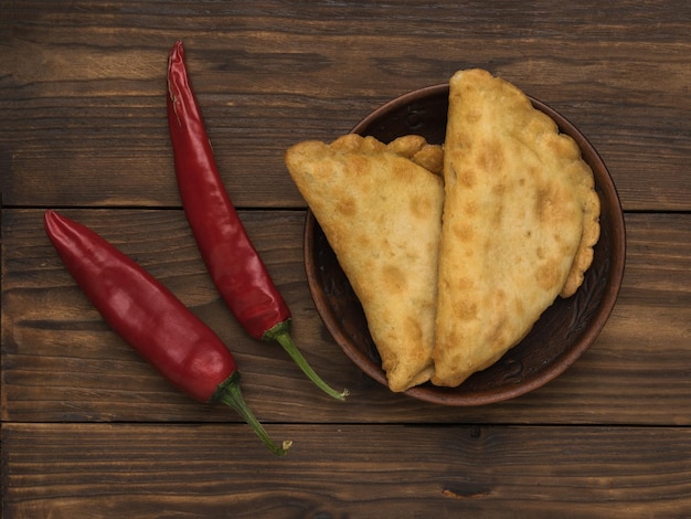 Dos vainas de pimiento rojo y pasteles fritos sobre una mesa de madera