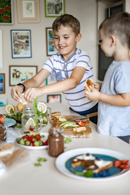 Dos varones hermano pequeño amigos decorar sándwich matutino con frutas y bayas de pasta de chocolate