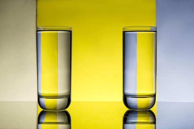 Dos vasos con agua sobre fondo gris y amarillo.