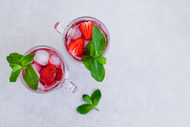 Dos vasos de bebida de fresa de verano con menta sobre un fondo claro