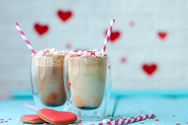 Dos vasos de café caliente o capuchino con malvaviscos y galletas en forma de corazón sobre un fondo de madera azul claro. Día de San Valentín de vacaciones.