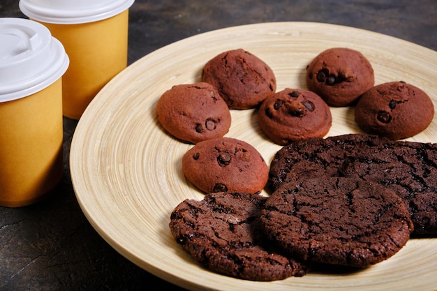 Foto dos vasos de café para llevar y una galleta americana sobre fondo oscuro.