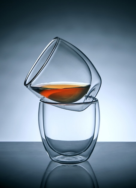 Dos vasos para café o té, uno encima del otro con té en el vaso superior con reflejo