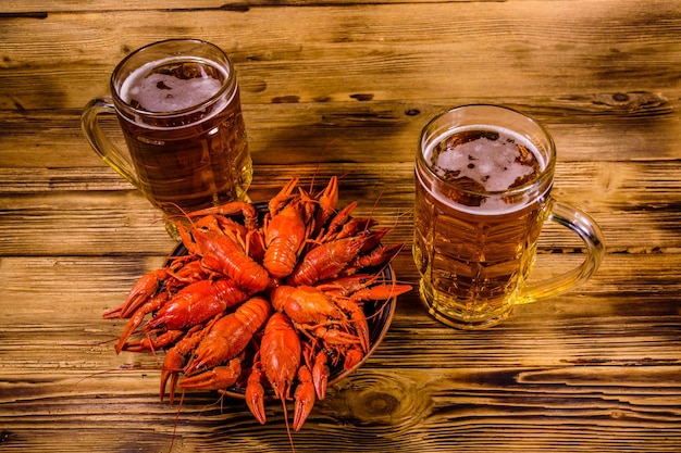 Dos vasos de cerveza y cangrejos de río hervidos en la mesa de madera