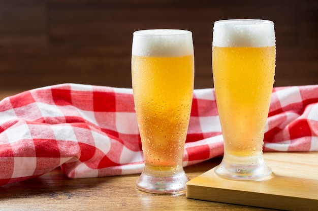 Dos vasos de cerveza espumosa contra una toalla plaid sobre mesa de madera