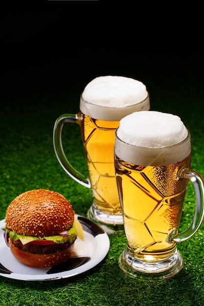 Dos vasos de cerveza y hamburguesas sobre hierba verde