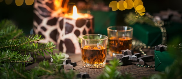Dos vasos de chupito de whisky o bourbon con decoración navideña sobre fondo de madera. Concepto de estado de ánimo de whisky de año nuevo, Navidad y vacaciones de invierno