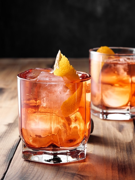 Dos vasos con un cóctel Negroni sobre una mesa de madera. Foto vertical.