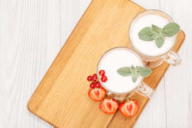 Dos vasos de delicioso yogur de fresa con hojas de menta y fresas frescas