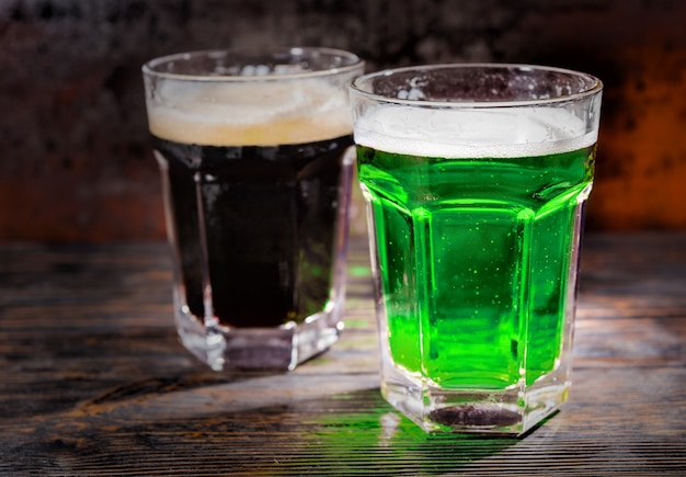 Dos vasos grandes con cerveza verde y oscura recién vertida en un escritorio de madera. Concepto de alimentos y bebidas