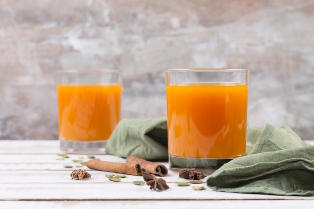 Dos vasos de jugo de calabaza, especias, canela y anís estrellado. Fondo gris borroso