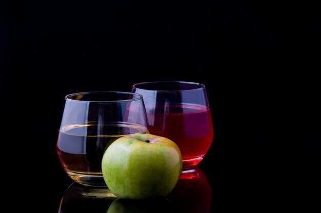 Dos vasos de jugo y una manzana sobre un fondo negro.