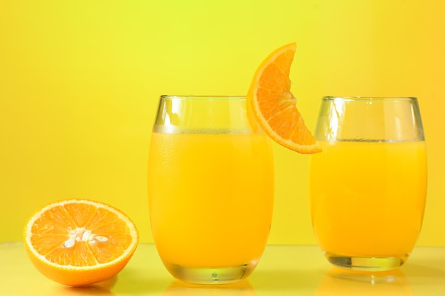 Dos vasos con jugo de naranja media naranja junto al vaso sobre el fondo amarillo