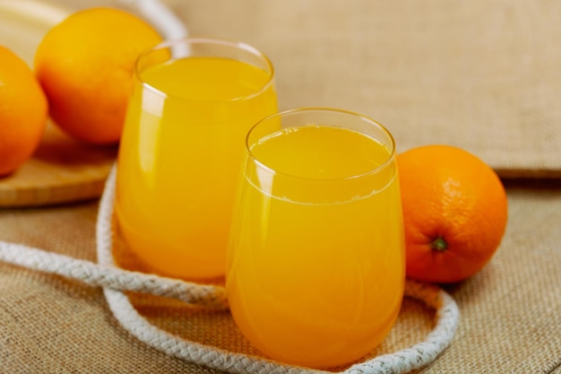 Dos vasos de jugo con naranjas alrededor.