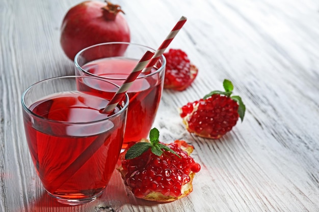 Dos vasos de jugo sabroso y fruta granate sobre fondo de madera