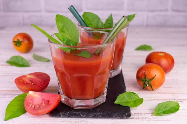 Dos vasos de jugo de tomate y hojas de albahaca fresca sobre un fondo blanco.