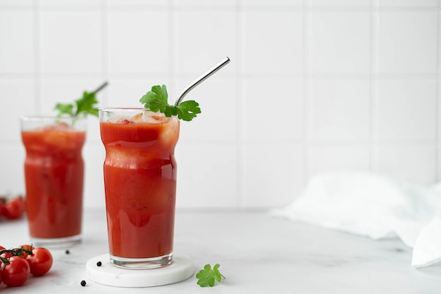 Dos vasos de jugo de tomate con una ramita de perejil sobre una mesa blanca