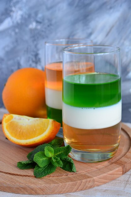 dos vasos con leche de kiwi y gelatina de naranja en la tabla de cortar de madera