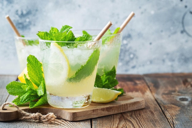 Dos vasos con limonada o cóctel mojito con limón y menta bebida refrescante fría o bebida con hielo sobre fondo azul rústico Copiar espacio