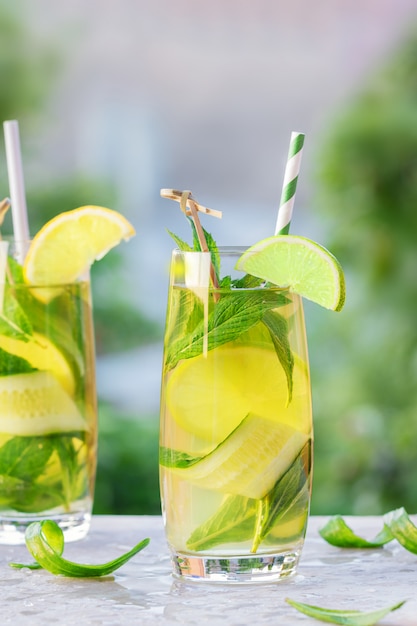 Dos vasos de limonada o cóctel mojito con limón, pepino y menta, bebida refrescante fría o bebida con hielo y paja de papel, al aire libre. Concepto de verano Agua fría de desintoxicación, copia espacio.