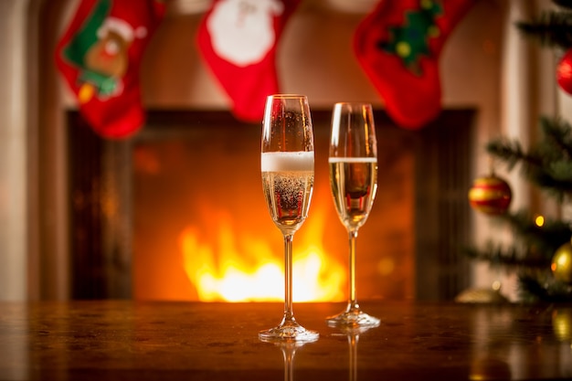 Dos vasos llenos de champán en la mesa de Navidad delante de la chimenea